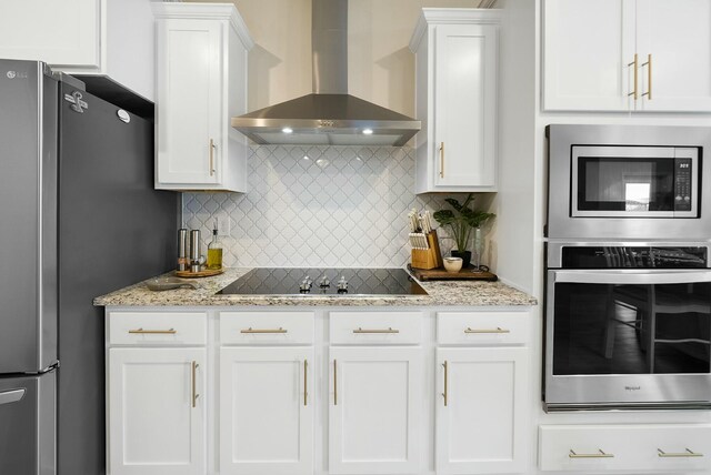 kitchen featuring tasteful backsplash, white cabinetry, stainless steel appliances, and wall chimney range hood