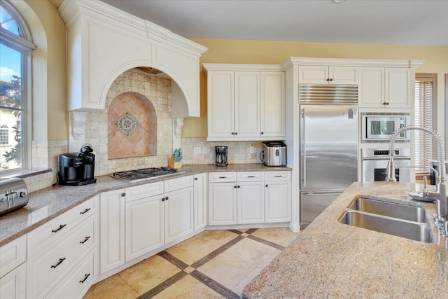 kitchen with decorative backsplash, built in appliances, white cabinetry, and sink