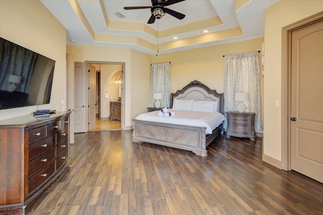 bedroom with a raised ceiling, ceiling fan, dark hardwood / wood-style flooring, and connected bathroom