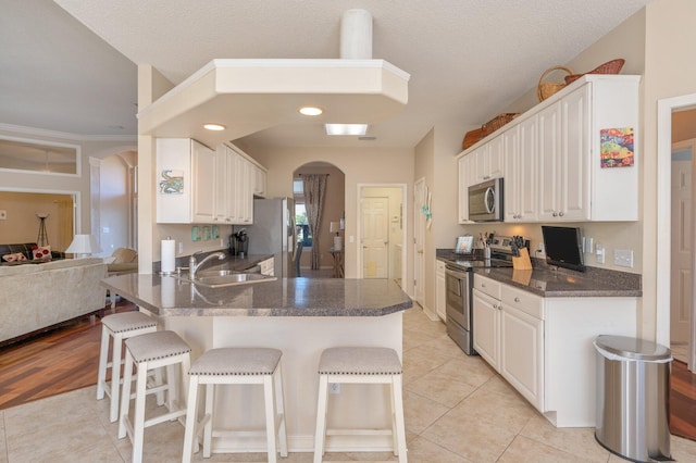 kitchen with white cabinetry, sink, kitchen peninsula, appliances with stainless steel finishes, and light wood-type flooring