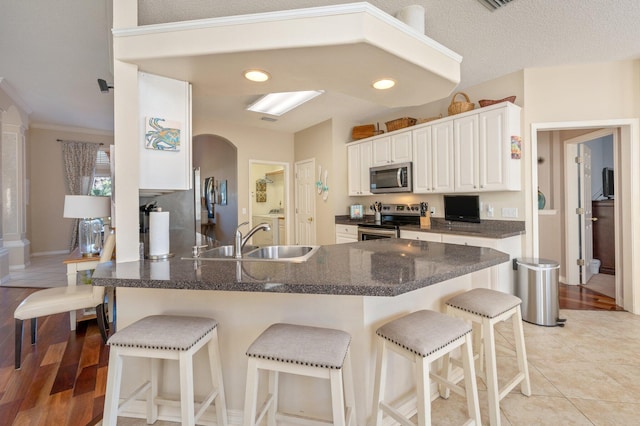 kitchen featuring sink, white cabinetry, light hardwood / wood-style floors, kitchen peninsula, and stainless steel appliances