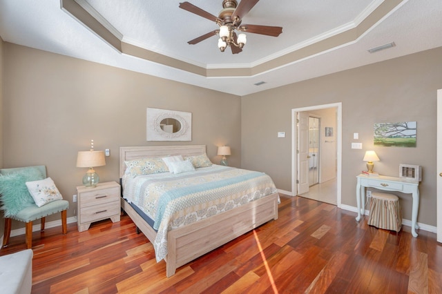 bedroom with ceiling fan, a raised ceiling, ornamental molding, and dark wood-type flooring