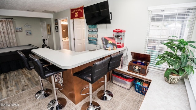 kitchen with kitchen peninsula, a breakfast bar, a textured ceiling, hardwood / wood-style flooring, and billiards