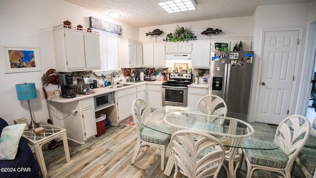 kitchen with decorative backsplash, appliances with stainless steel finishes, sink, white cabinets, and light hardwood / wood-style floors