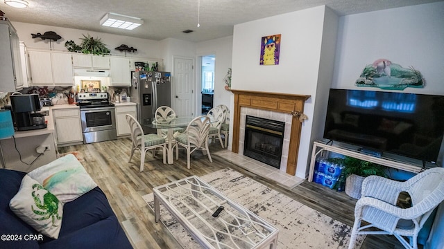 living room featuring a tiled fireplace, a textured ceiling, and light wood-type flooring