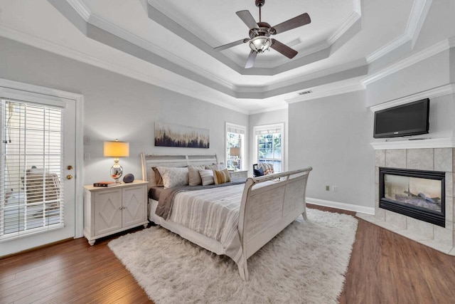 bedroom with visible vents, a tiled fireplace, ornamental molding, wood finished floors, and a tray ceiling