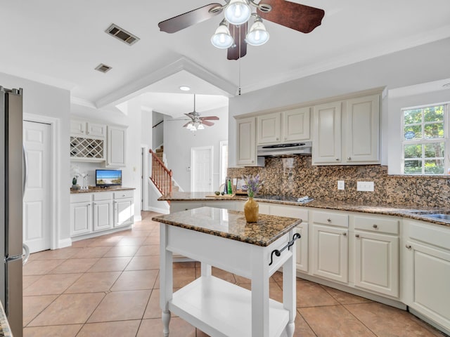 kitchen with visible vents, backsplash, stone countertops, freestanding refrigerator, and under cabinet range hood