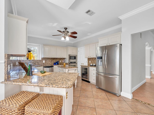 kitchen featuring a peninsula, appliances with stainless steel finishes, white cabinets, and light stone countertops