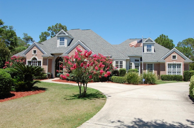 view of front facade with brick siding, a front lawn, and roof with shingles