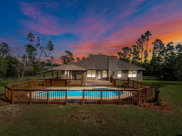 pool at dusk featuring a patio and a lawn