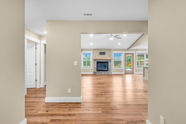 unfurnished living room featuring light wood-type flooring, a stone fireplace, ceiling fan, and lofted ceiling