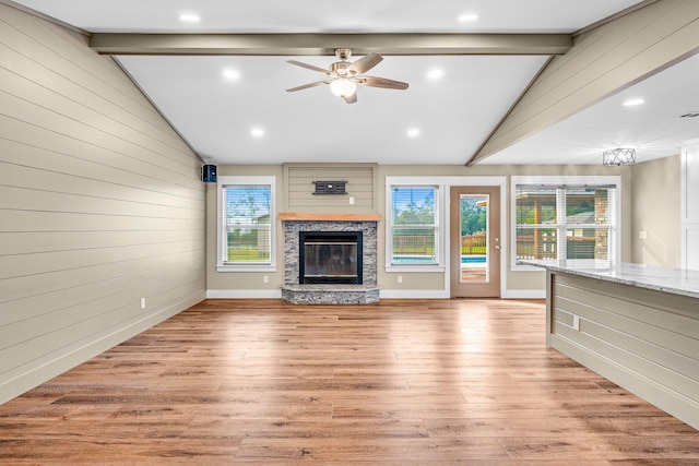 unfurnished living room with a stone fireplace, lofted ceiling with beams, ceiling fan with notable chandelier, and light hardwood / wood-style floors