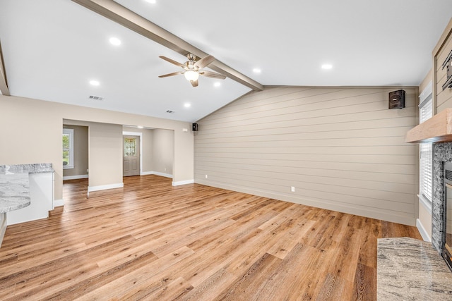 unfurnished living room with vaulted ceiling with beams, light hardwood / wood-style flooring, ceiling fan, and wood walls