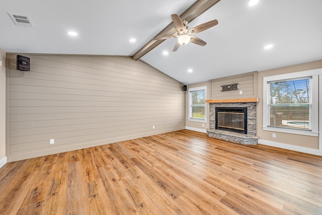 unfurnished living room with light wood-type flooring, ceiling fan, lofted ceiling with beams, a stone fireplace, and wood walls