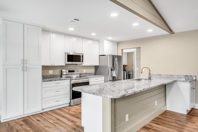 kitchen with kitchen peninsula, light stone counters, stainless steel appliances, sink, and white cabinets