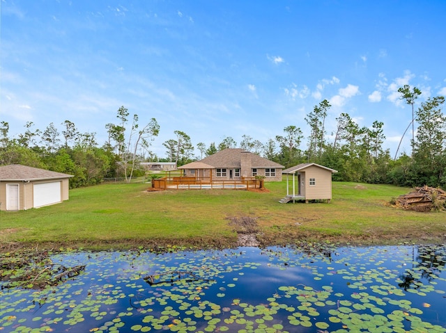 rear view of property featuring a lawn, a deck with water view, a garage, and a storage unit