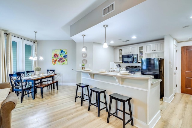 kitchen featuring black appliances, a kitchen breakfast bar, white cabinets, decorative light fixtures, and light hardwood / wood-style floors