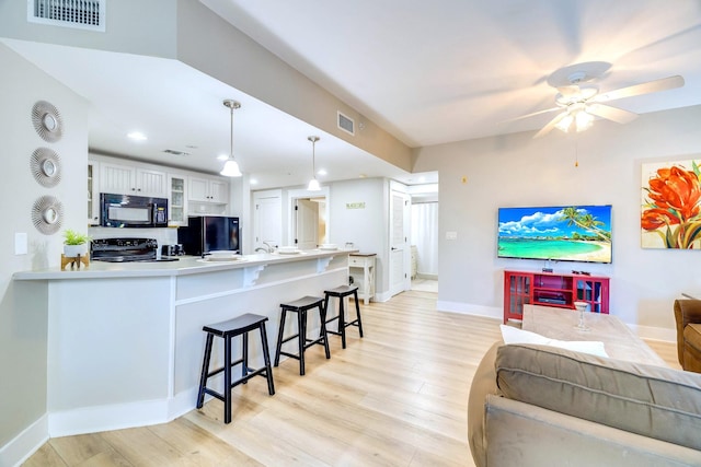 kitchen featuring pendant lighting, black appliances, white cabinets, light wood-type flooring, and kitchen peninsula