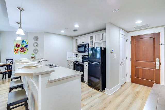 kitchen with sink, black appliances, light hardwood / wood-style flooring, white cabinets, and hanging light fixtures