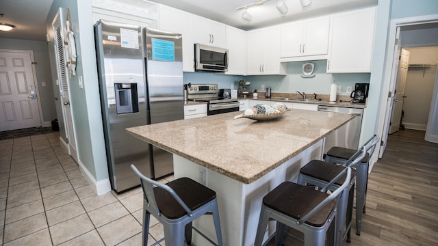 kitchen with light stone counters, stainless steel appliances, white cabinets, a center island, and a breakfast bar area