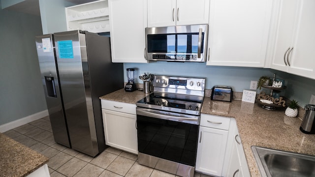 kitchen featuring white cabinets, appliances with stainless steel finishes, light tile patterned floors, and dark stone countertops