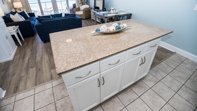 kitchen with white cabinets, a center island, light stone counters, and light hardwood / wood-style floors