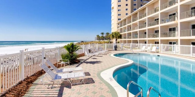 pool with a patio, a beach view, fence, and a water view