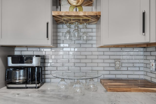 kitchen featuring light stone counters, white cabinets, and backsplash