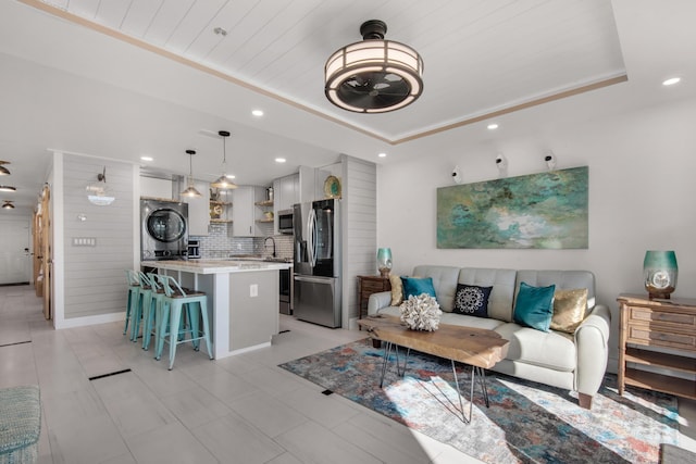 living room with a tray ceiling, stacked washing maching and dryer, wood ceiling, and recessed lighting