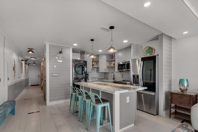 kitchen with light stone counters, open shelves, stacked washer / drying machine, visible vents, and appliances with stainless steel finishes