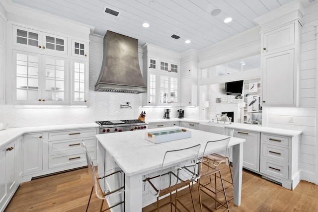 kitchen with light stone counters, a breakfast bar, custom range hood, light hardwood / wood-style flooring, and white cabinets