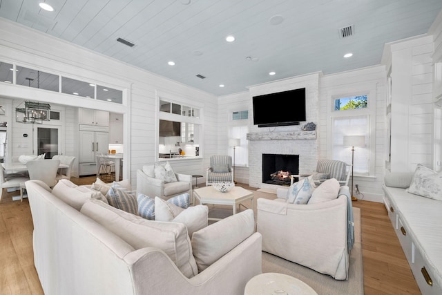 living room featuring wooden ceiling, a large fireplace, light hardwood / wood-style floors, and ornamental molding