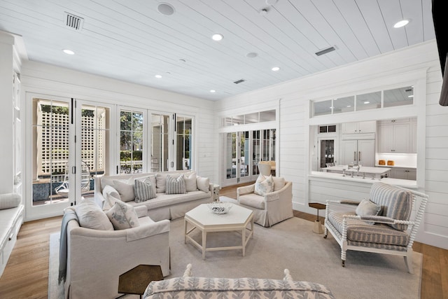 living room with french doors, light hardwood / wood-style flooring, and wood walls