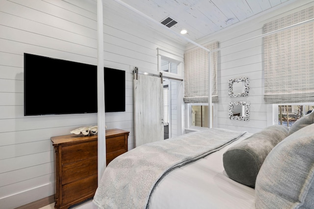 bedroom featuring a barn door, wood walls, wooden ceiling, and hardwood / wood-style flooring