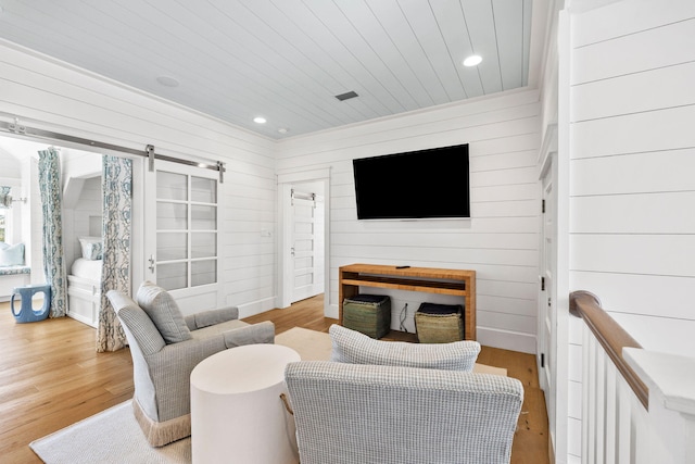 living room with a barn door, wood walls, and light hardwood / wood-style flooring