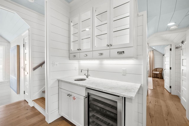 bar featuring white cabinets, vaulted ceiling, light hardwood / wood-style floors, light stone counters, and beverage cooler