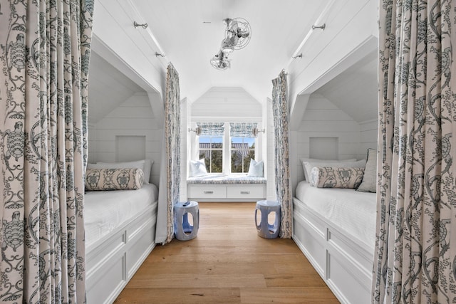 bedroom with wooden walls, vaulted ceiling, and light wood-type flooring