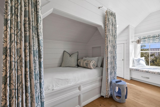 bedroom with wood walls, vaulted ceiling, and light wood-type flooring