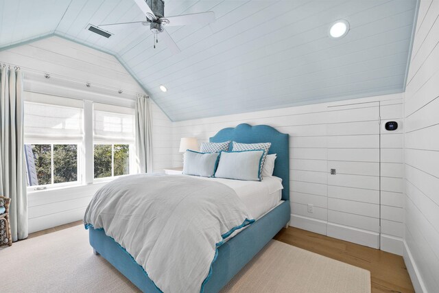 bedroom with wooden walls, light hardwood / wood-style floors, ceiling fan, and lofted ceiling