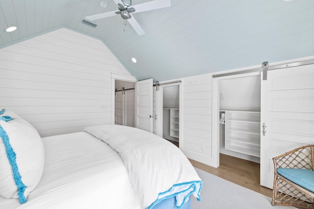 bedroom featuring wood-type flooring, a barn door, vaulted ceiling, and ceiling fan