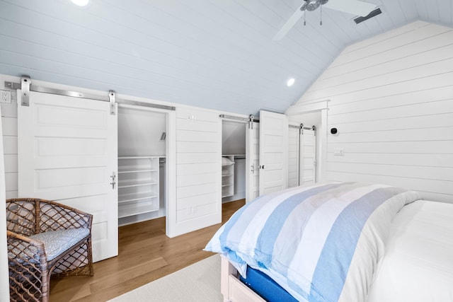 bedroom with ceiling fan, a barn door, hardwood / wood-style floors, vaulted ceiling, and a walk in closet