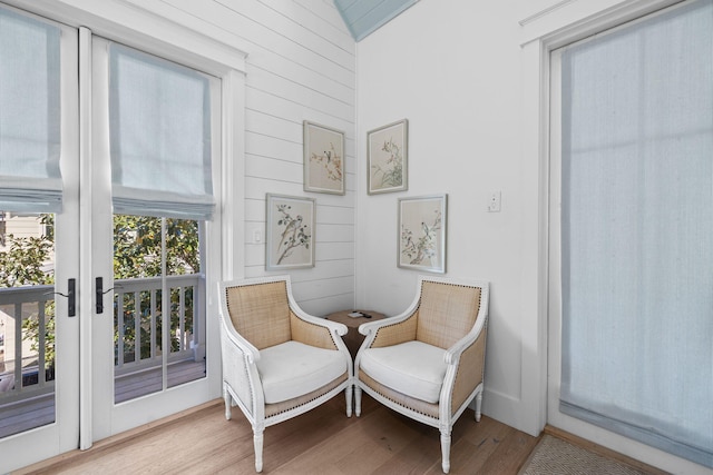 sitting room featuring wooden walls, french doors, vaulted ceiling, and light wood-type flooring