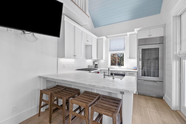 kitchen featuring kitchen peninsula, sink, light hardwood / wood-style flooring, white cabinetry, and a breakfast bar area