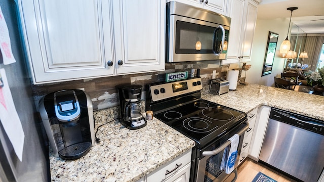 kitchen featuring light stone countertops, tasteful backsplash, decorative light fixtures, white cabinetry, and stainless steel appliances