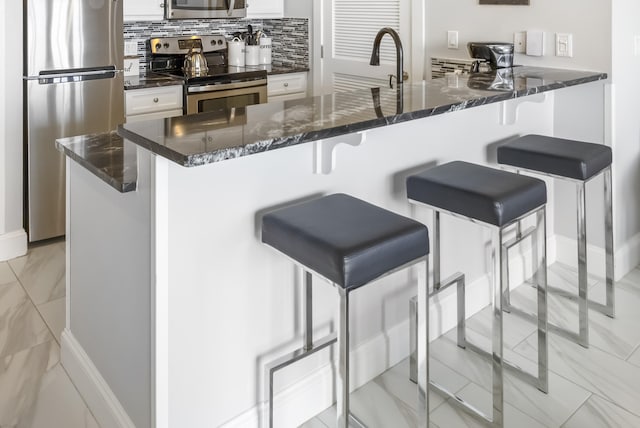 kitchen featuring backsplash, white cabinets, a kitchen breakfast bar, appliances with stainless steel finishes, and kitchen peninsula