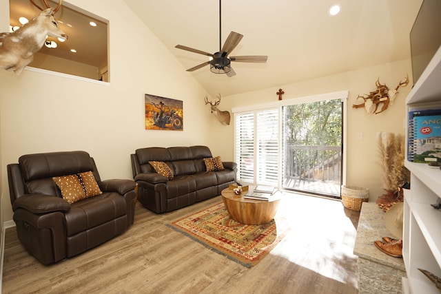 living room with wood-type flooring, high vaulted ceiling, ceiling fan, and a stone fireplace