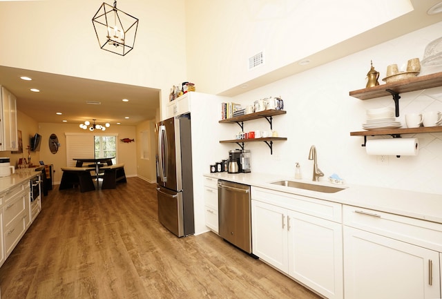 kitchen with sink, light hardwood / wood-style floors, decorative light fixtures, white cabinets, and appliances with stainless steel finishes