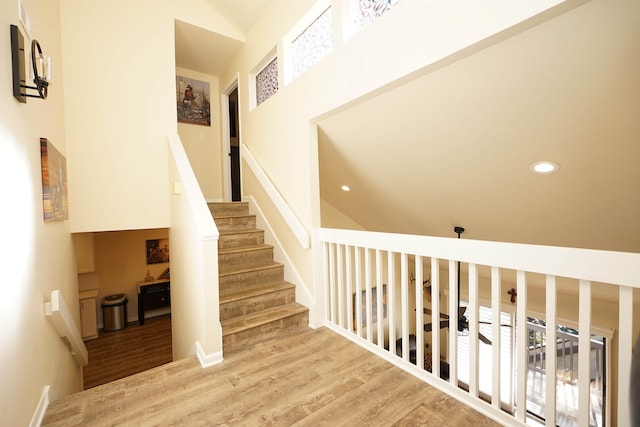 stairway featuring ceiling fan, high vaulted ceiling, and wood-type flooring