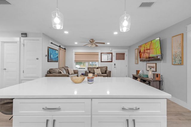 kitchen featuring white cabinets, a barn door, light hardwood / wood-style floors, and hanging light fixtures