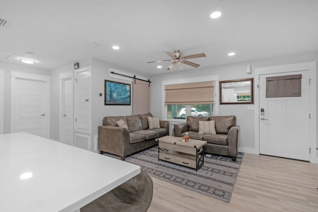 living room featuring a barn door, light hardwood / wood-style flooring, and ceiling fan